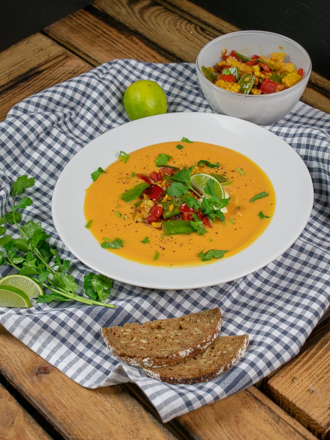 Vegane Süßkartoffelsuppe schön serviert mit Pfannengemüse zur Seite, Limette und Koriander