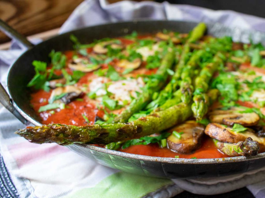 Shakshuka mit grünem Spargel in der Gusseisenpfanne