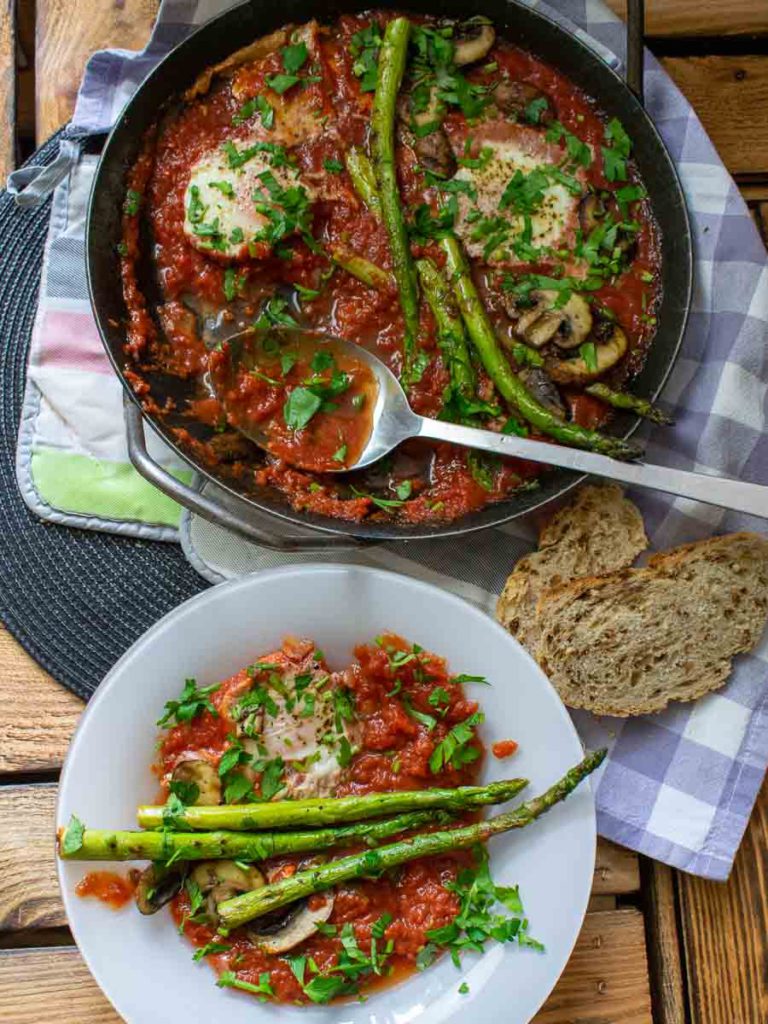 Shakshuka mit grünem Spargel angerichtet auf tiefem Teller